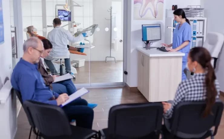 Modern dental clinic office with dentist using laptop to manage SEO and ads while friendly staff assist patients in reception