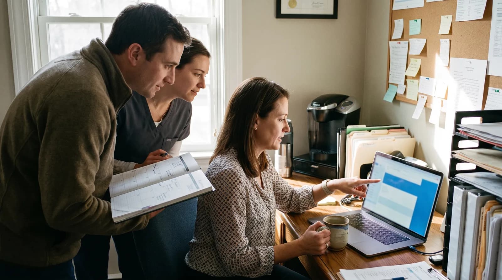 Dental team gathered around a laptop and appointment planner, scheduling time away for a dental conference